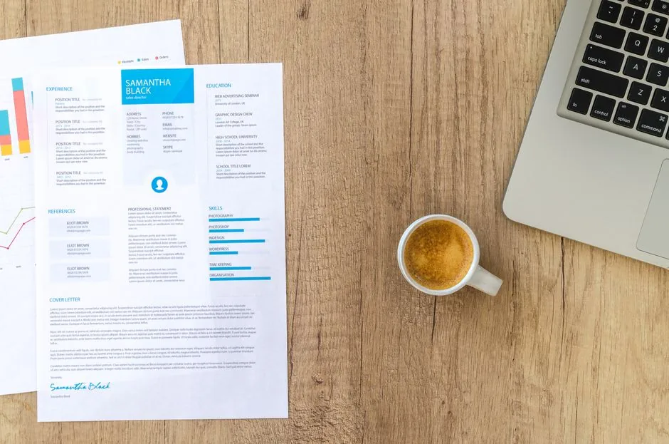 Top view of a desk with resume, coffee cup, and laptop on a wooden surface, ideal for business concepts.
