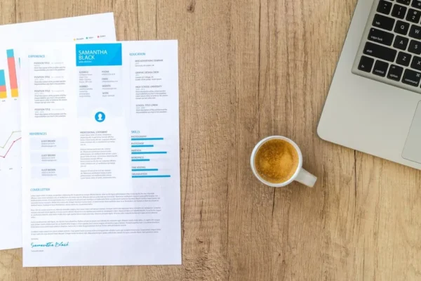 Top view of a desk with resume, coffee cup, and laptop on a wooden surface, ideal for business concepts.